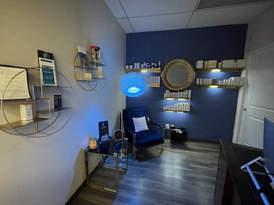 Chameleon Medical Spa Consult Room A room with blue walls, a chair in the corner and light from a stylish lamp